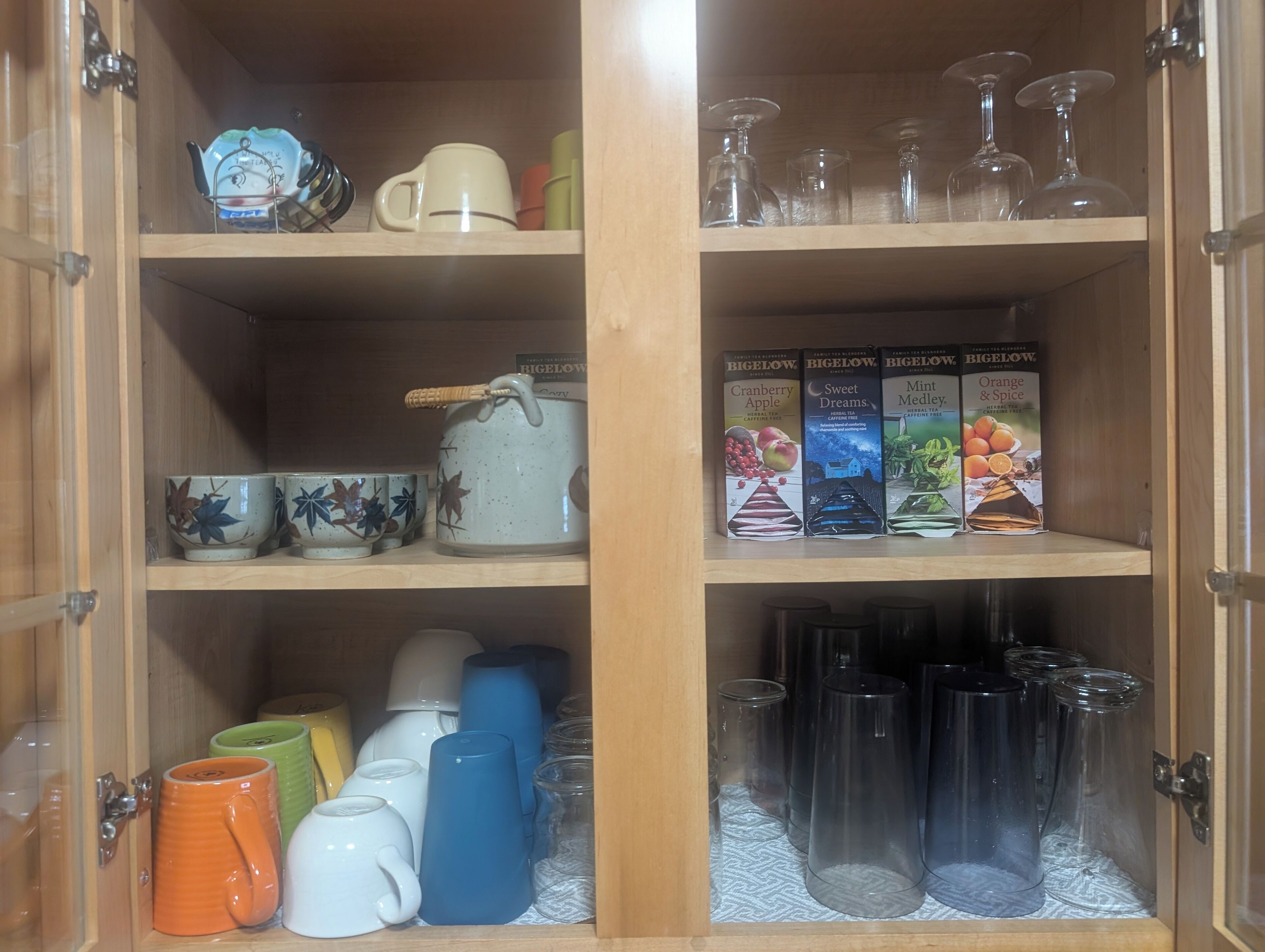 Un meuble en bois doté d’étagères contenant diverses boîtes à thé, des tasses en céramique et de la verrerie.