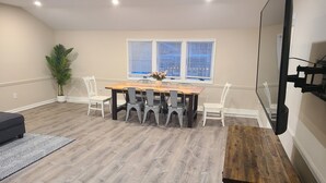 A spacious room with a wooden dining table surrounded by chairs, a potted plant, and a large window with blinds. - Downtown Marblehead 2brm/1.5bath w/ deck (Marblehead)