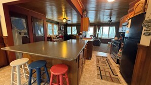 Una cocina con una isla grande, armarios de madera, un refrigerador y un comedor con sofá y sillas.