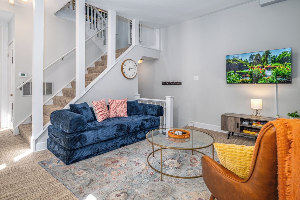 A living room with a blue sofa, a round coffee table, a staircase, and a wall-mounted TV.