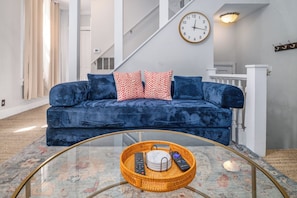 A living room with a blue sofa, a glass coffee table, and a wall clock.
