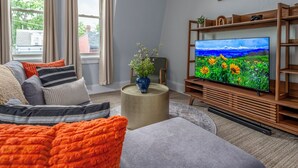 A living room with a large flat-screen TV, a sofa, a coffee table with a vase, and a bookshelf. - Prime Mt Adams+Lux Beds+Sleeps 6ppl+Deck Views+Smart TVs+Spacious Living Rooms (Cincinnati)
