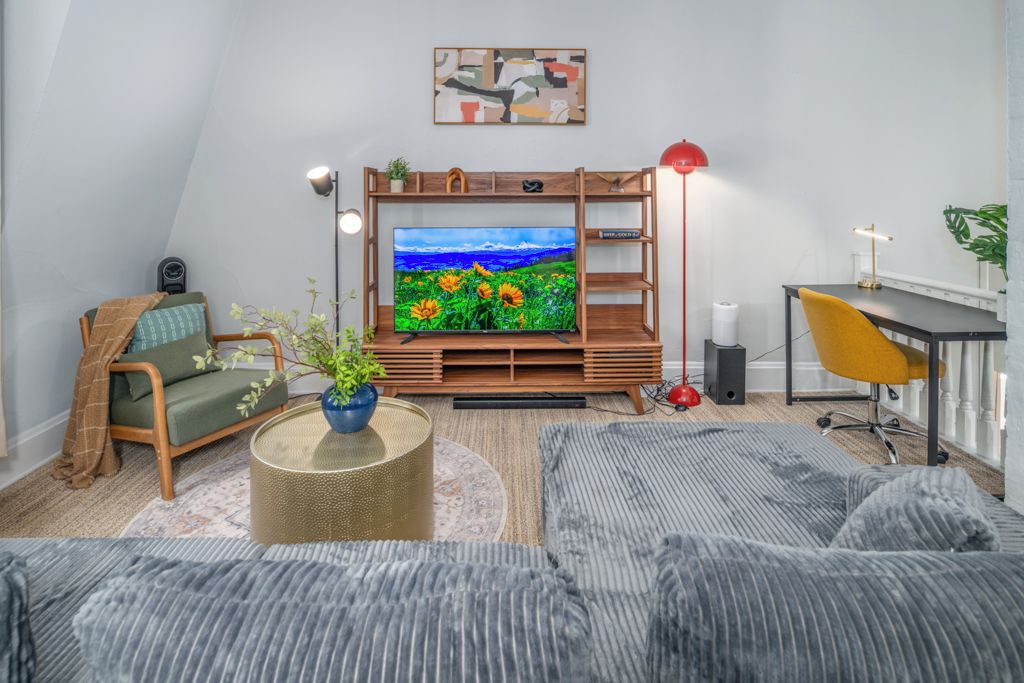 Een moderne woonkamer met een flatscreen televisie, een bank, een bureau en een rode vloerlamp.