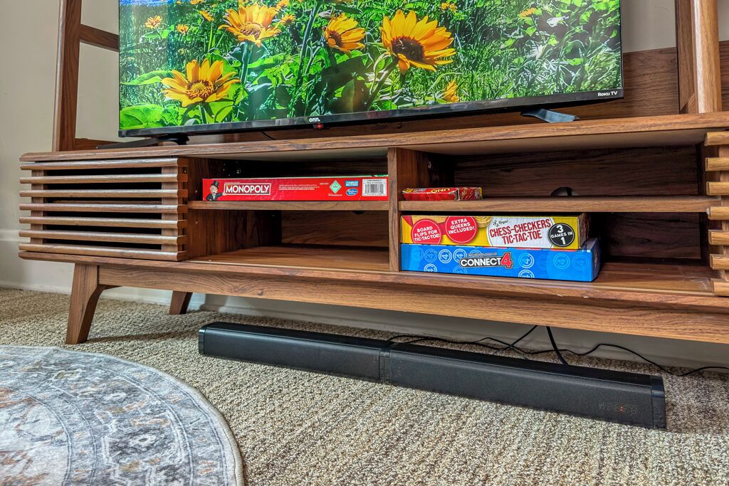 A wooden entertainment center with a television displaying a nature scene, a Monopoly game box, and a Connect4 game box.