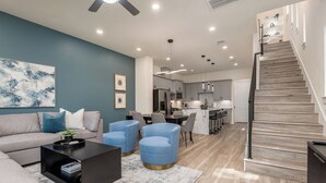 A modern living room with a grey sofa, blue armchairs, a black coffee table, and a staircase leading to a kitchen area. - 3-bedroom house in welcoming Houston with WiFi, AC, EV Charging (Houston)