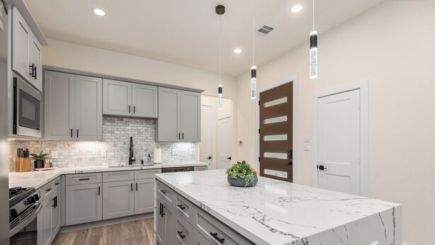 A modern kitchen with grey cabinets, a white marble island, and pendant lighting. - 3-bedroom house in welcoming Houston with WiFi, AC, EV Charging (Houston)