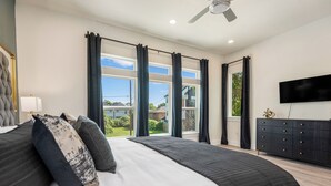A modern bedroom with a large bed, a flat-screen TV, and a view of the outdoors. - 3-bedroom house in welcoming Houston with WiFi, AC, EV Charging (Houston)