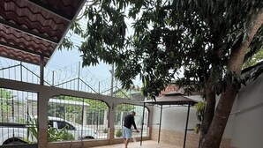 A covered outdoor area with a tiled floor, a tree, and a metal fence. - Charming 2-bedroom house with AC, WiFi in enjoyable and expacious house (Cantón Quitasol)