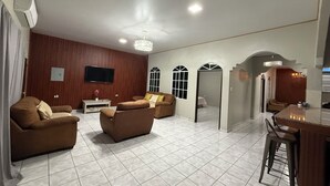 A spacious living room with a large TV, two sofas, a coffee table, and a dining area with a bar counter. - Charming 2-bedroom house with AC, WiFi in enjoyable and expacious house (Cantón Quitasol)