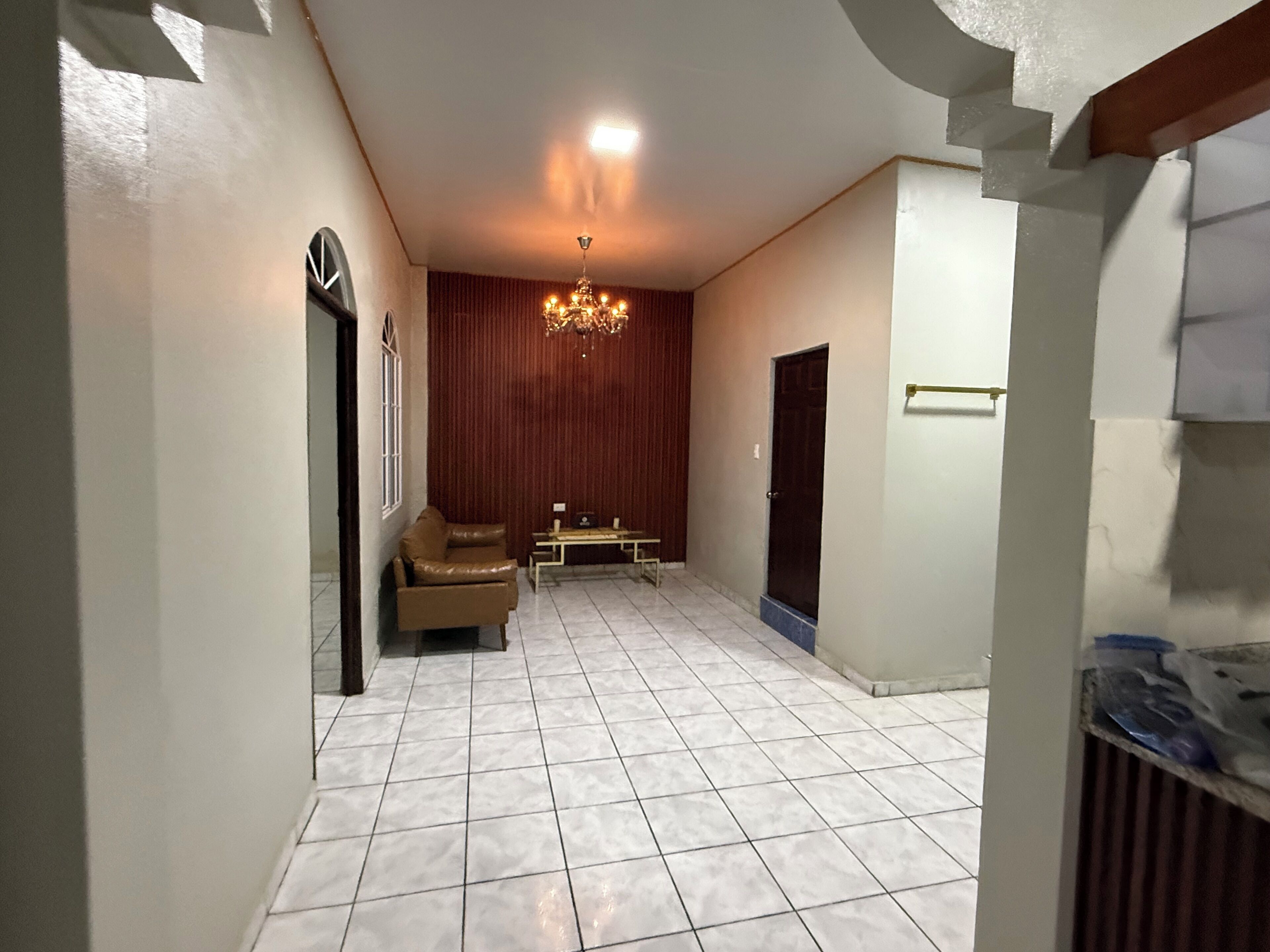 A spacious hallway with a tiled floor, a brown leather sofa, a small table, and a chandelier.