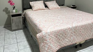 A bedroom with a bed, a nightstand, a small table, and a potted plant. - Charming 2-bedroom house with AC, WiFi in enjoyable and expacious house (Cantón Quitasol)