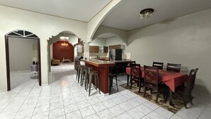 A spacious living area with a kitchen, a dining area with a red tablecloth, and a hallway leading to another room. - Charming 2-bedroom house with AC, WiFi in enjoyable and expacious house (Cantón Quitasol)
