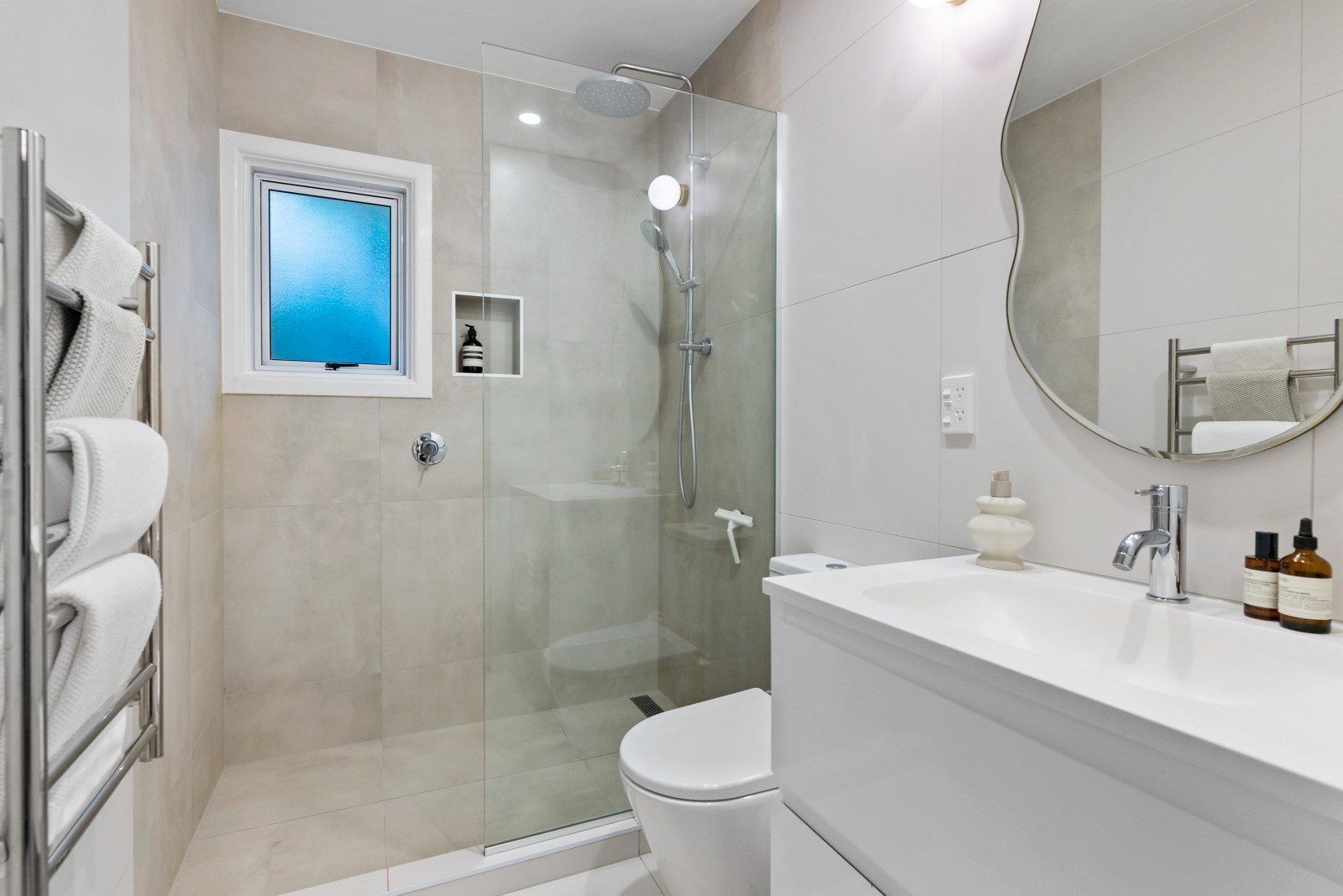 A modern bathroom with a glass-enclosed shower, a white sink, and a large mirror.