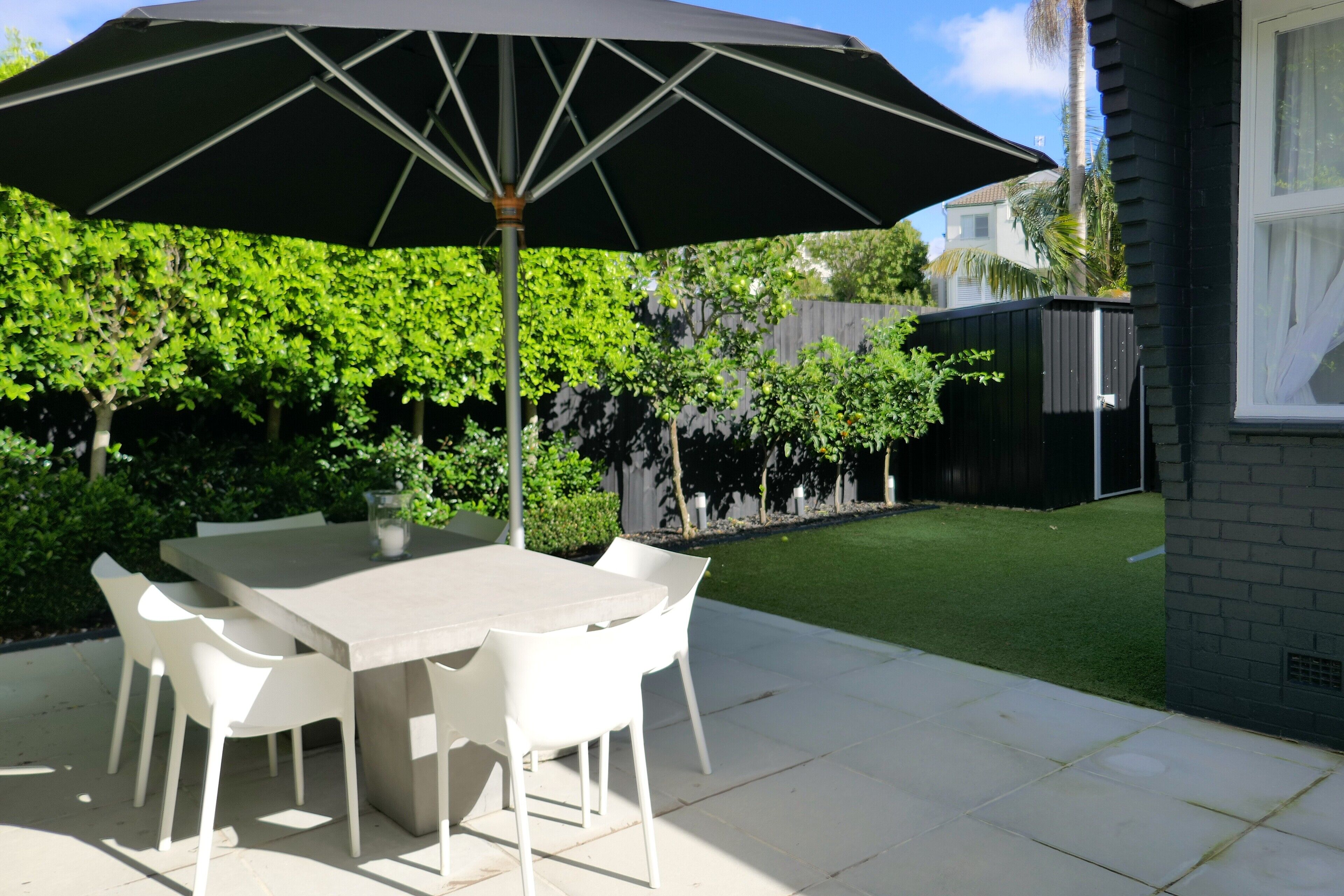 A patio with a table and chairs, an umbrella, and a well-maintained lawn.
