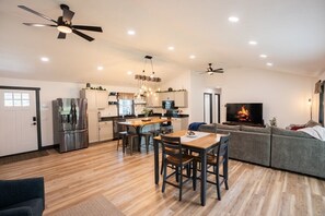 Une cuisine moderne avec un îlot central, un coin repas avec des chaises, un canapé et un téléviseur diffusant une image de feu de cheminée.