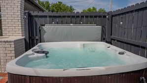 Un jacuzzi con plataforma de madera y pared de ladrillo al fondo.