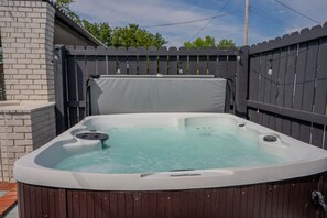 A hot tub with a wooden deck and a brick wall in the background.