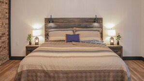 Una cama bien hecha con una colcha a rayas, dos lámparas de noche y un cabecero de madera.