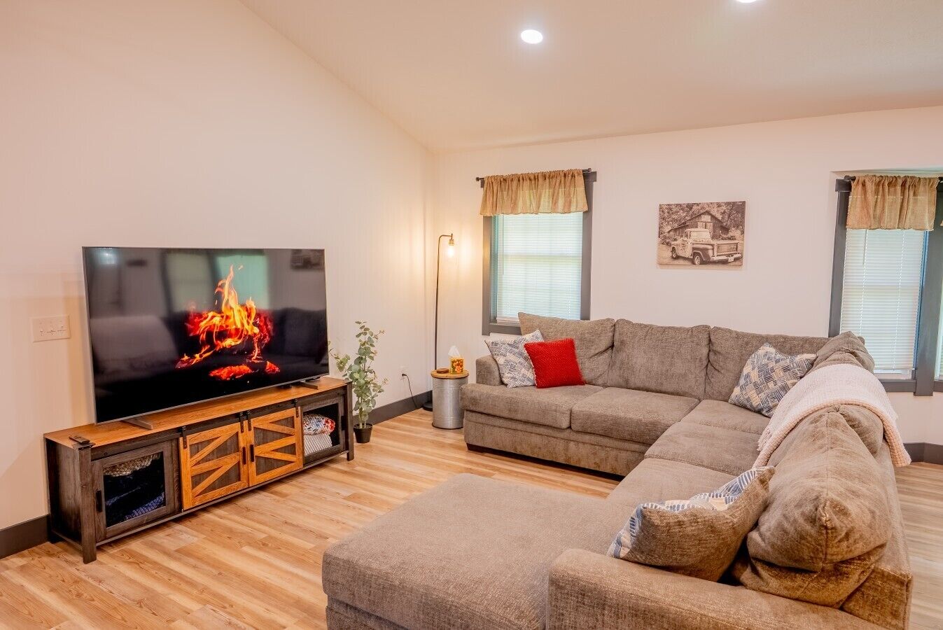 Uma sala de estar com televisão de tela plana, sofá seccional, móvel para entretenimento de madeira e luminária de chão.