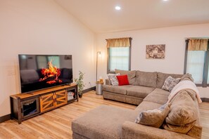 A living room with a flat-screen TV, a sectional sofa, a wooden entertainment unit, and a floor lamp.