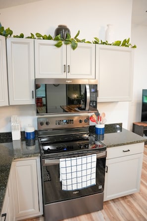 A kitchen with white cabinets, a stainless steel microwave, oven, and a granite countertop.