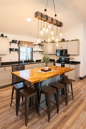 A modern kitchen with a wooden island, bar stools, and pendant lighting.