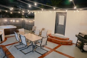 An outdoor patio with a table and chairs, a hot tub, and a grill area.