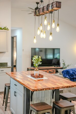 A modern kitchen with a wooden island, bar stools, a TV, and a unique ceiling light fixture.