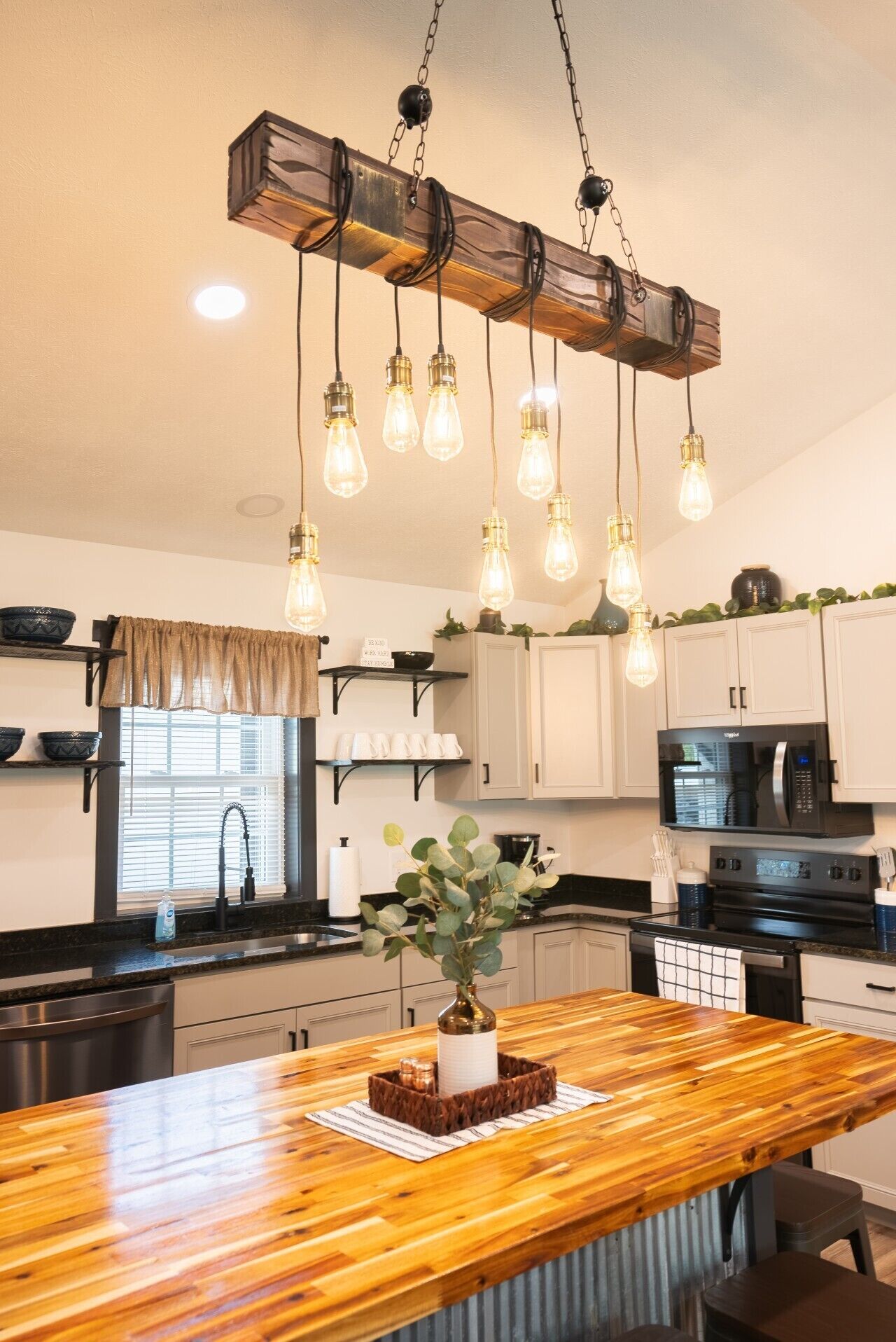 A kitchen with a wooden island, hanging light fixtures, and white cabinets.