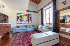 A living room with a sofa, ottoman, and a colorful geometric artwork on the wall.