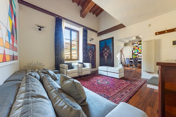 A living room with a sofa, chairs, a red rug, and artwork on the walls.
