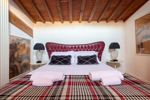 A hotel room with a red upholstered headboard, a plaid bedspread, two bedside lamps, and artwork on the walls.