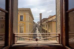 A view from a window overlooking a narrow street with buildings, a bell tower, and a bridge.