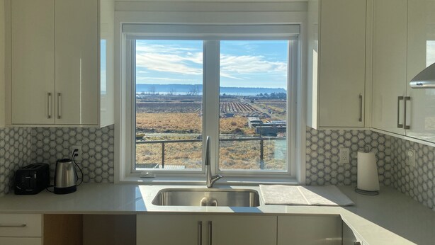 A kitchen with a large window, white cabinets, a stainless steel sink, and a toaster. - Panorama ridge suite (Surrey)