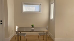 A dining area with a rectangular table, two chairs, a small potted plant, and a window above the table. - Panorama ridge suite (Surrey)