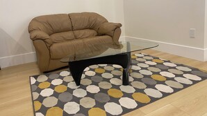 A living room with a brown leather sofa, a glass-top coffee table, and a patterned rug. - Panorama ridge suite (Surrey)