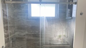 A modern bathroom with a glass-enclosed shower, a toilet, and a small window above the shower. - Panorama ridge suite (Surrey)
