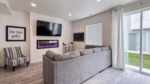 A modern living room with a grey sofa, a striped armchair, a flat-screen TV, and a fireplace.