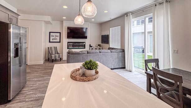 A modern kitchen with a central island, a dining table with chairs, and a living area with a sofa and TV.