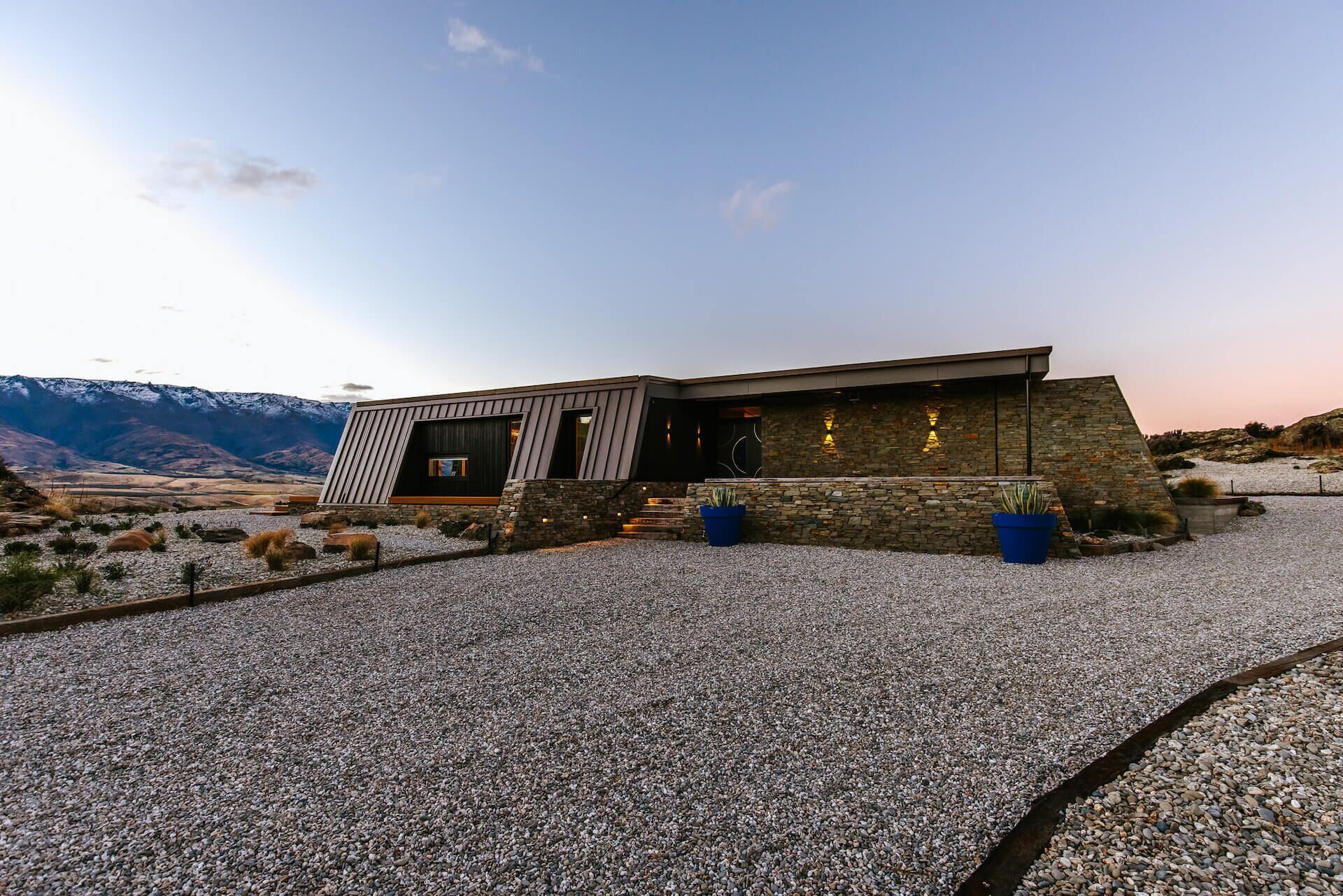 A modern house with a stone facade, large windows, and a gravel driveway.