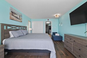 A bedroom with a bed, dresser, TV, and a painting on the wall.