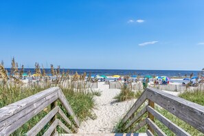 A wooden pathway leading to a beach with umbrellas and beach chairs.