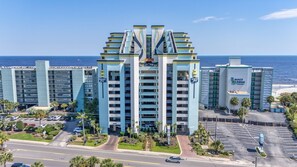 A multi-story hotel with a central atrium, parking lot, and ocean view.