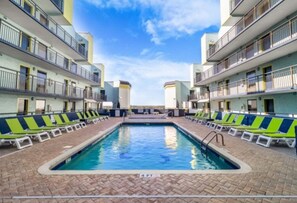 Una piscina con sillones de descanso a ambos lados, rodeada de edificios de varios pisos con balcones.