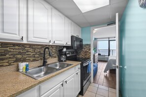 A kitchen with white cabinets, a granite countertop, a black faucet, and a coffee maker.