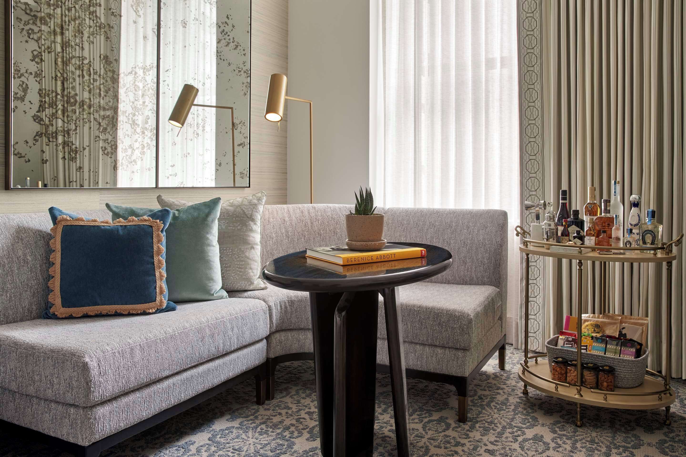 A modern living room with a grey sofa, a round coffee table, and a decorative plant. A multi-tiered side table with various items is visible.