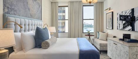 A hotel room with a large bed, a desk, a chair, a dresser, and a view of the cityscape.