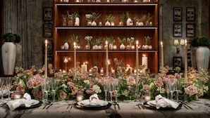 A well-lit dining area with a wooden bookshelf, floral centerpieces, and candles.