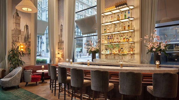 A bar area with a long counter, multiple bar stools, and a well-stocked shelf with various bottles.