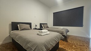 A hotel room with two beds, a nightstand, a lamp, and a large window. - STAY Hydra Comfort Apartment (Nicosia)